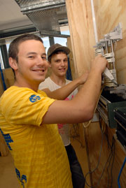 Two student working on a wall mounted circuit