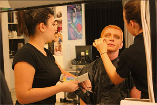 Two student applying makeup to model