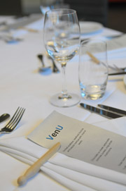 Close view of white tablecloth with wine and water glass, silver cutlery, white napkins and menu with VenU logo