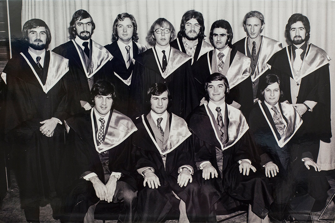 A group of 20-something men in graduation gowns with 1070s facial hair