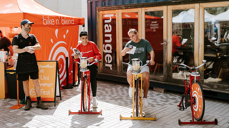 Three students riding stationary bicycles to blend smoothies