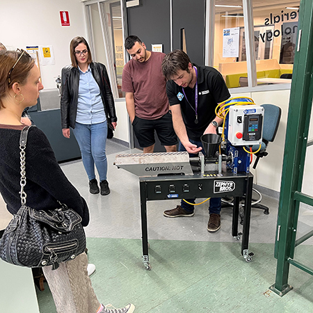 A man in Victoria University polo shirt demostrates a machine to onlookers