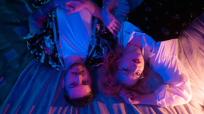 Head shot of young man and woman, lying on bed, in dreamy lighting, looking at camera
