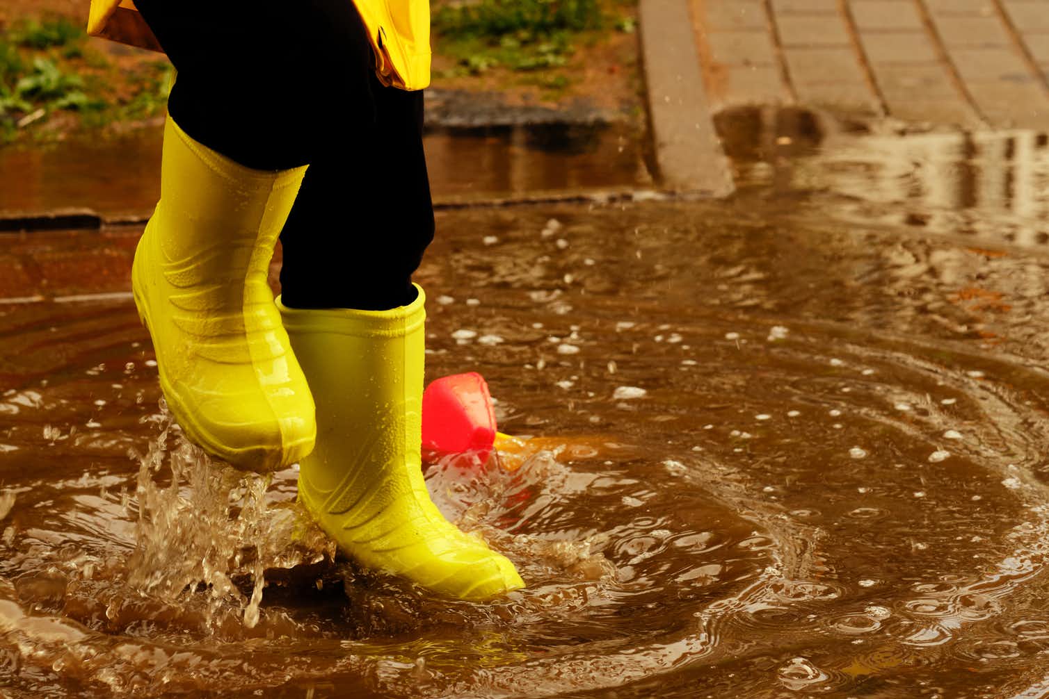 A child's legs, wearing yellow gumboots, splashing in a puddle.