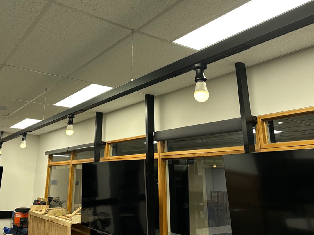  Four lightbulbs attached along a long black beam hanging from the ceiling. The lightbulbs are turned on.
