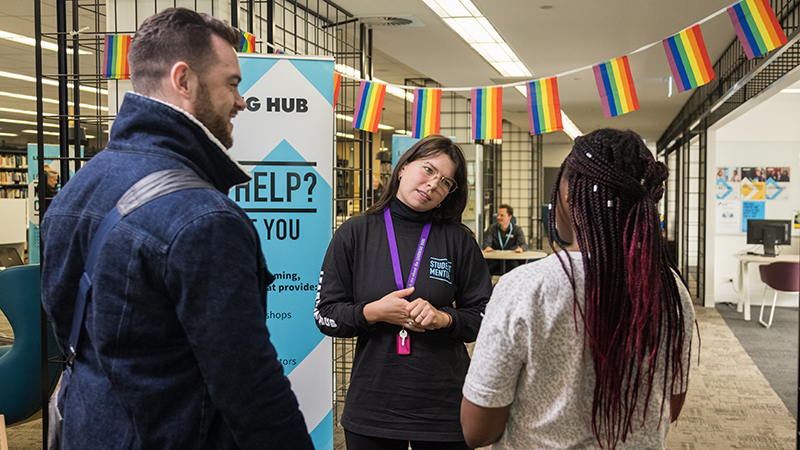 A student mentor listens attentively to 2 students arriving at a drop-in session