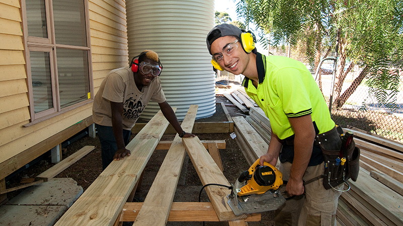 Carpentry students smiling and working on a hands-on project together. 