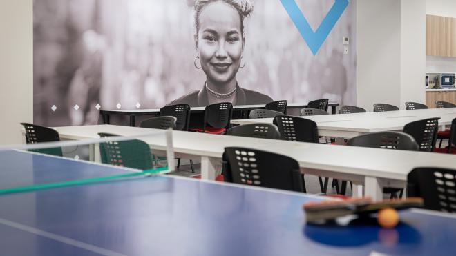 Students get access to a table tennis set in our break room. A table tennis racquet and ball sitting on a table tennis table. In the background are tables and chairs.