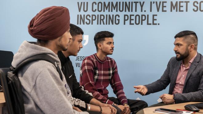 We offer student support on the ground floor of our campus. Four people sitting down. One person is talking to them, using their hands to make gestures, while the other three listen to them.