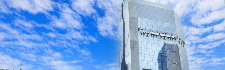 A modern glass tower with 'Victoria University' on it, against a blue sky