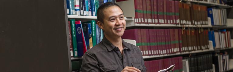 A man stands in a library and smiles.