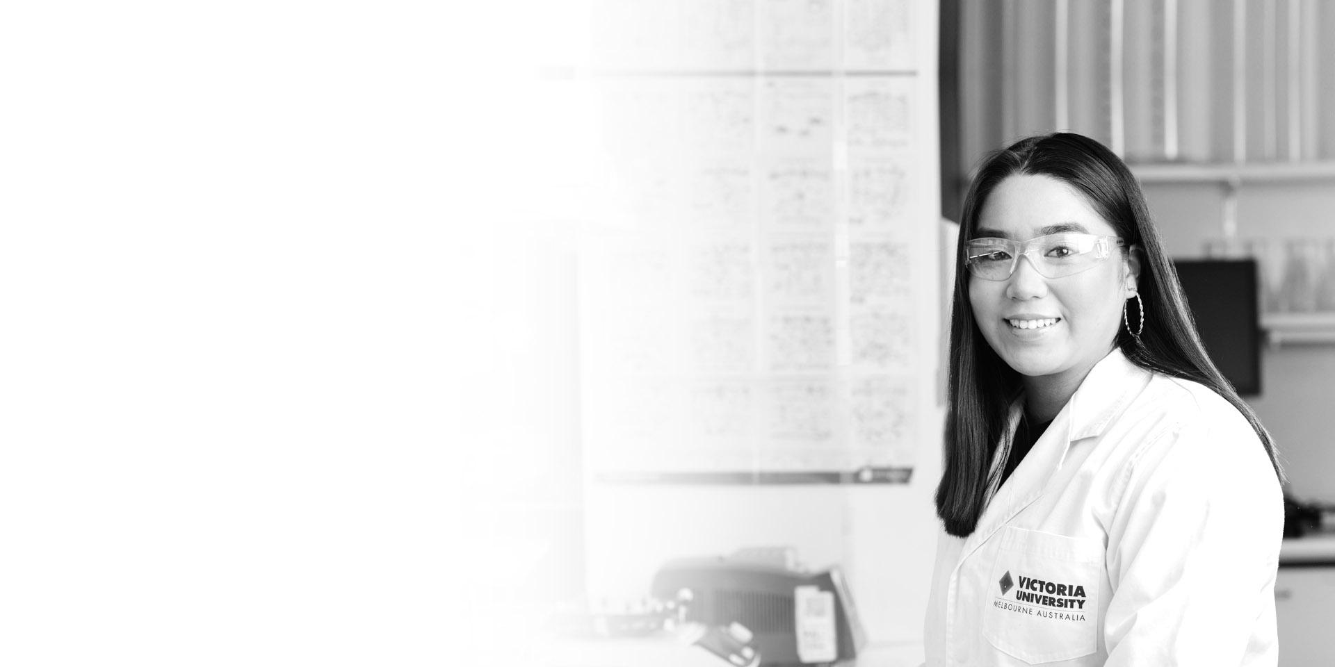  A research scholarship recipient in glasses and a lab coat with the VU logo on it.