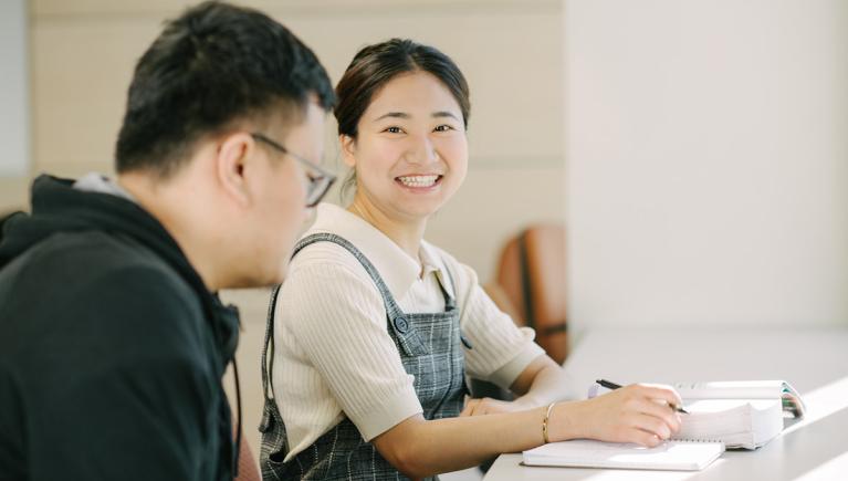 two young Asian students, studying, smiling at camera