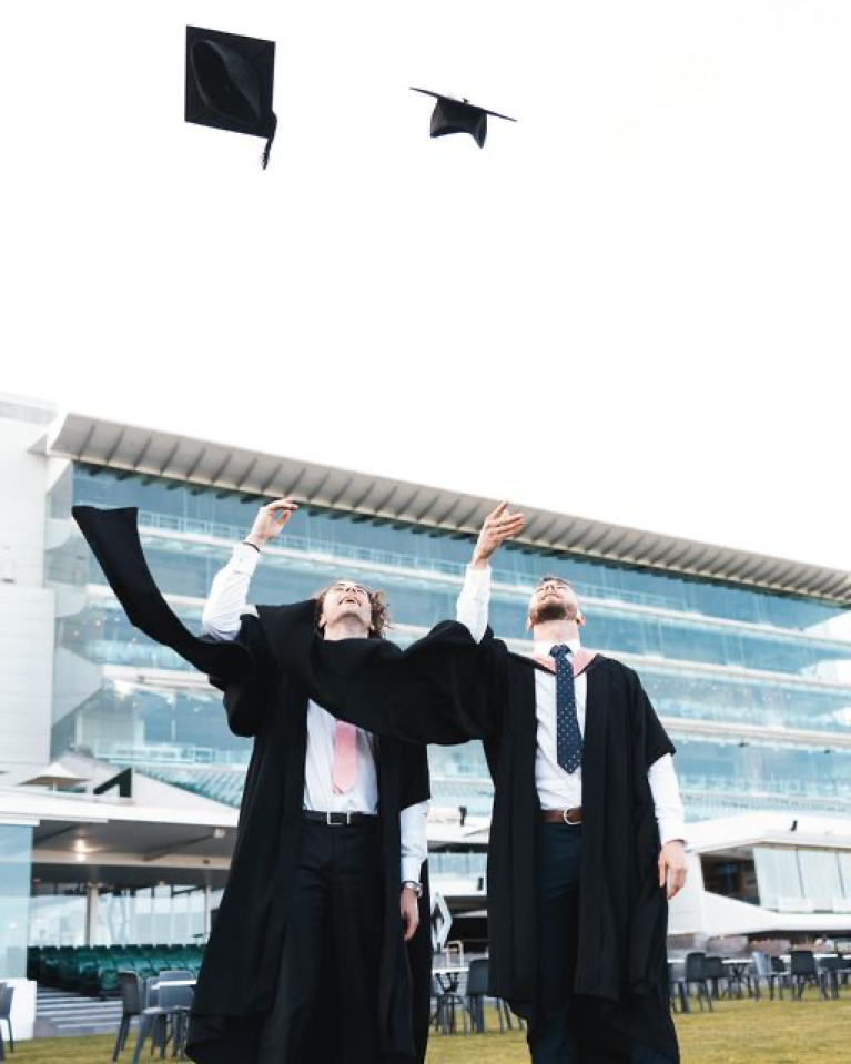  two graduates celebrating at Flemington Racecourse, throwing their caps in the air