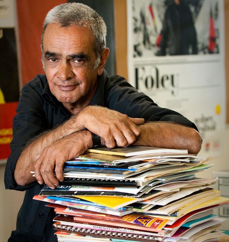 Professor Gary Foley leaning on a stack of paperwork for the Aboriginal History Archive