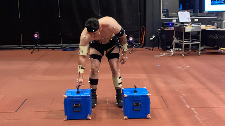  A person wearing electrodes reaches down to pick up a heavy load as part of a study.