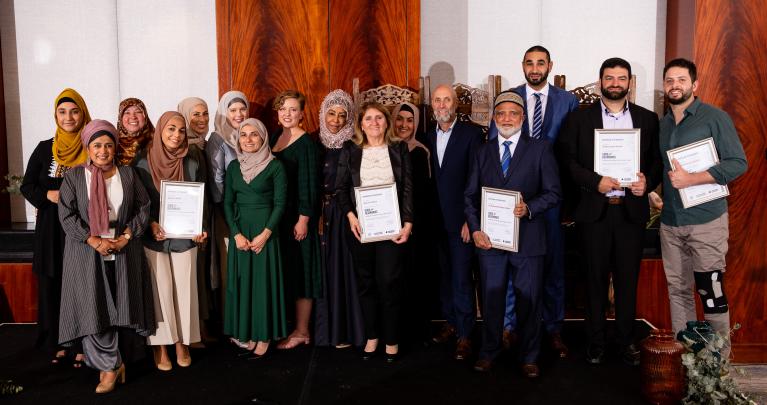 Marriage Mentors from the Pilot Program graduate, March 2022 Marriage Mentors and Program staff stand on stage and smile with graduation certificates.