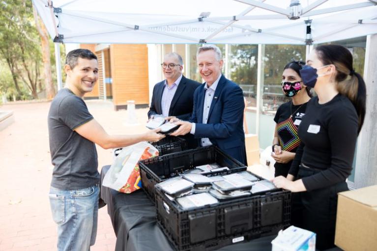  VU student Luciano Freire picks up free food packs from VC Adam Shoemaker and Deputy VC (People and Organisation) Peter Radoll, accompanied by VU students Shiva Foroutan and Ashlie Thorburn