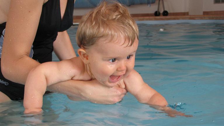 Baby happy in water, held by woman 