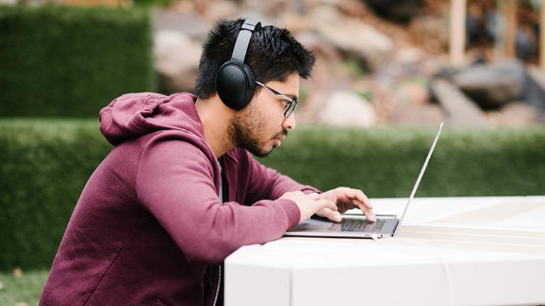  A student sitting outside, studying on a laptop with headphones on.