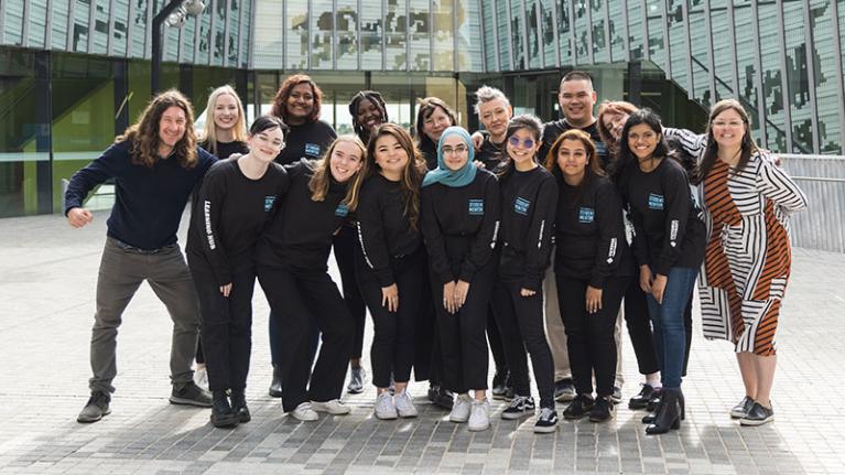 Group of students, multicultural, wearing mentor shirts, smiling in campus courtyard