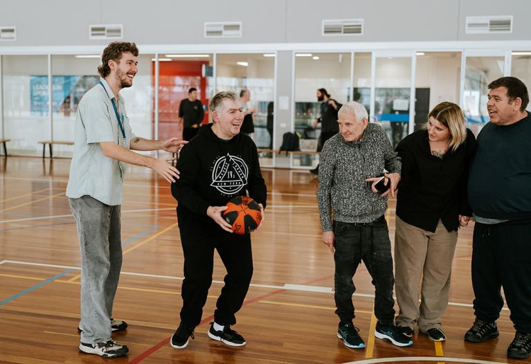 A young man assisting a group of adults with disability to play basketball