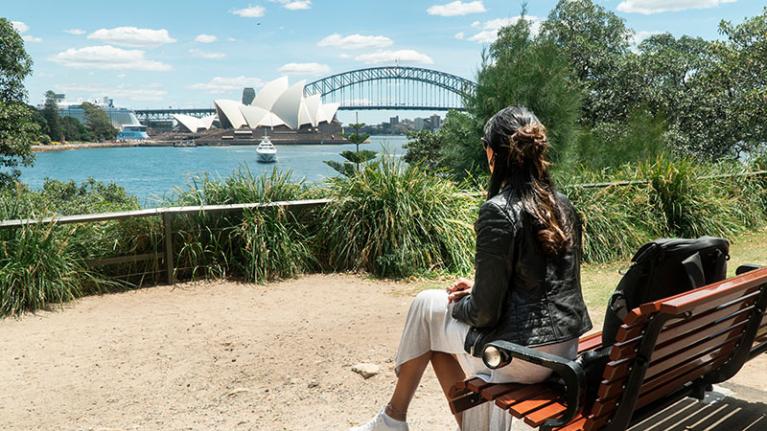  Aperson sits on a park bench looking at a view of Sydney Harbour Bridge and the Opera House.