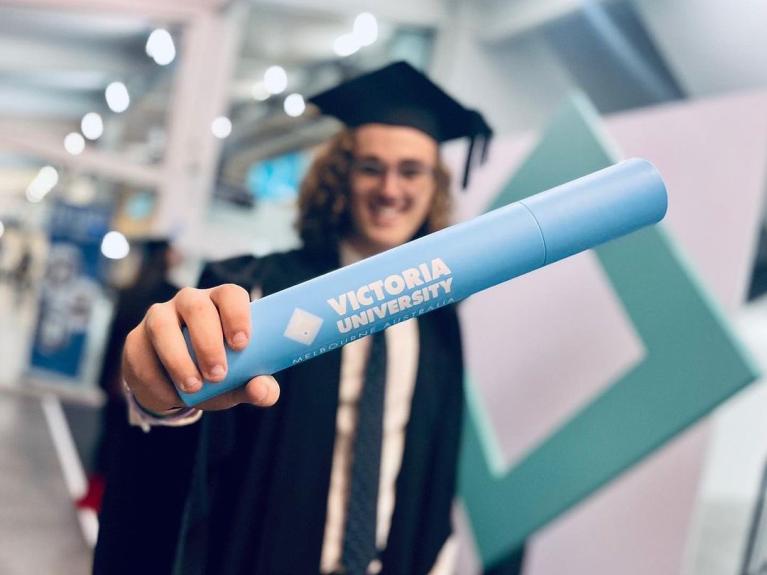  graduate proudly holding out his testamur in it's VU casing