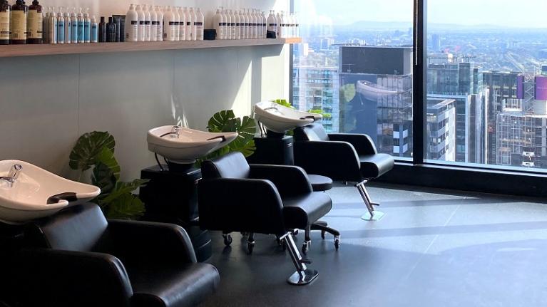  Three hairdressing chairs in the VU Moss salon at VU City Tower with a view of Melbourne in the window behind