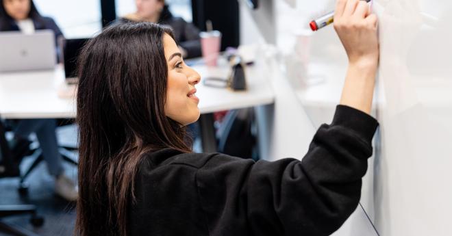 Young woman in a modern classroom writes on a whiteboard