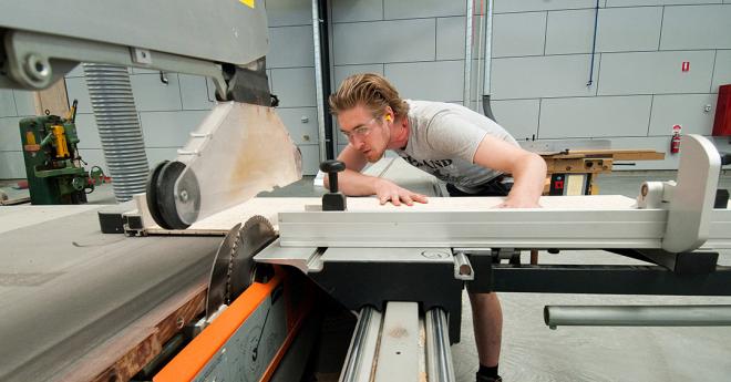 A young man in trade clothing operates large machinery