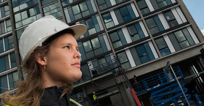 Emma Buis, engineering alumni, standing in front of skyscraper wearing construction hat.