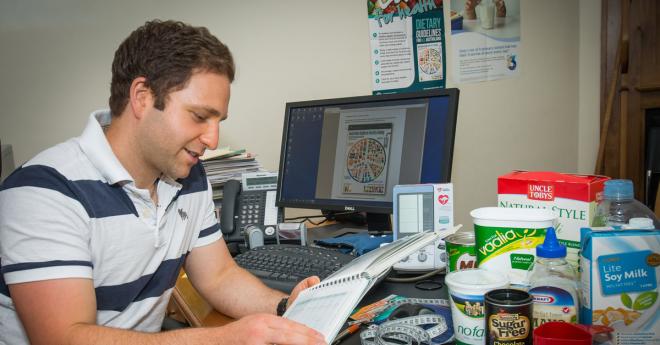 Master of Nutrition student at a computer desk with different foods and charts