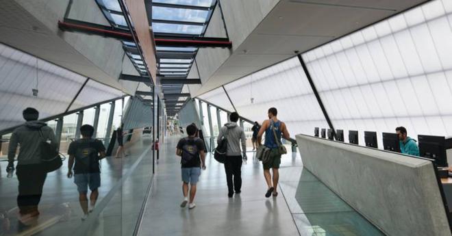 A group of students walk through a modern, light large passage, with a long row of skylights