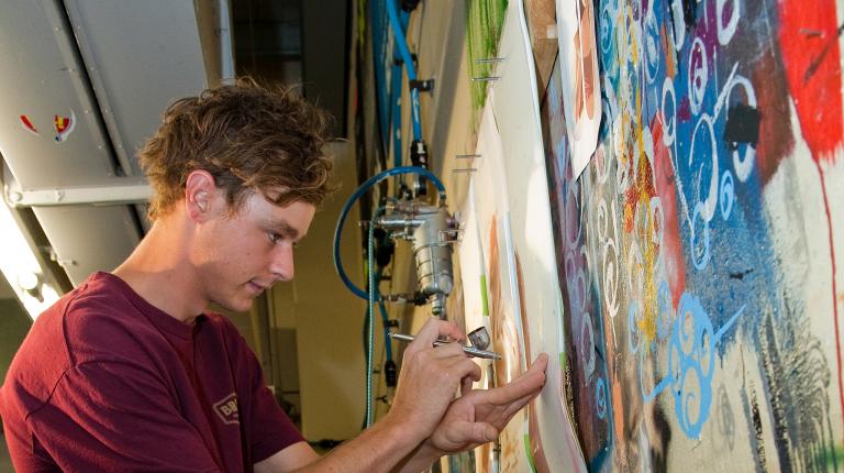 A person studying creative arts works on a mural.