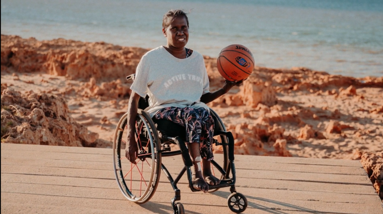 Aboriginal female wheelchair-basketball player, holding basketball at boardwalk sunny beach