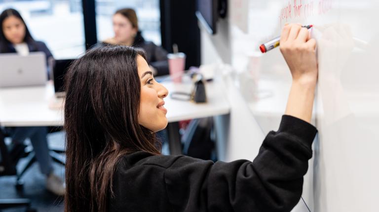 Young woman in a modern classroom writes on a whiteboard