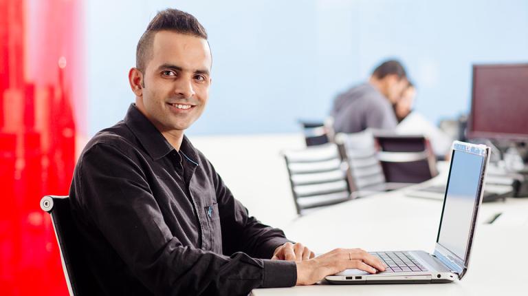  student smiling at camera, whilst working on a laptop