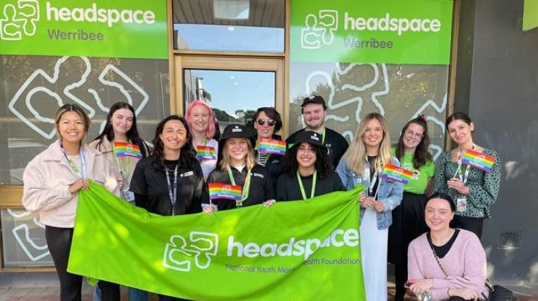 A group of young people with rainbow flags hold a green 'Headspace' banner