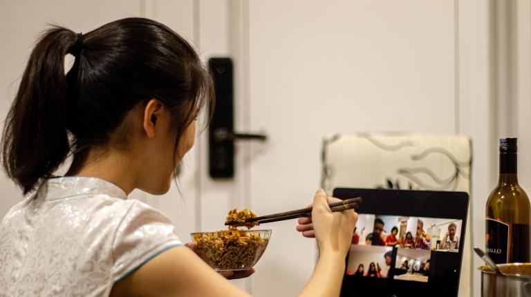 Woman eating chinese dinner whilst on a zoom chat.