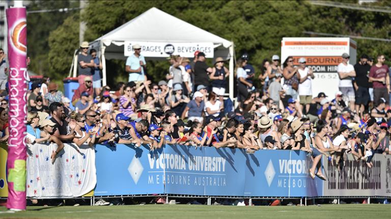 AFL crowd behind a Victoria University logo barrier