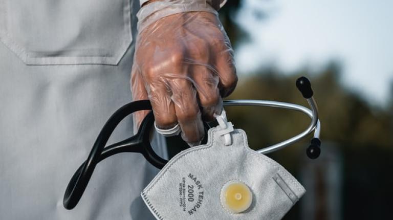 A gloved hand holding a mask and stethoscope