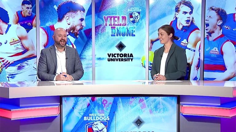 Sam Hargreaves and Ellie Blackburn discussing the VU Data Lab findings on the Finals Countdown Sam and Ellie behind a podium with lots of Victoria University and Western Bulldogs branding