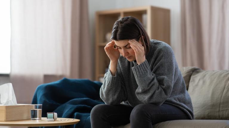 woman depressed on couch, holding head with pill bottle in front of her
