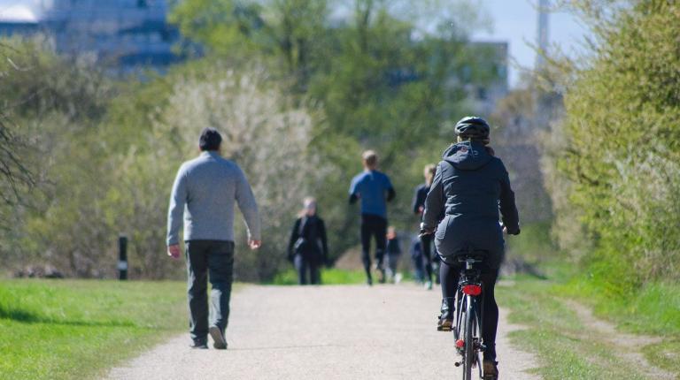  People in winter clothes walking and riding a bike in a park.