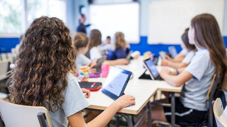 Primary school kids sitting as desks with tablets in a classroom.