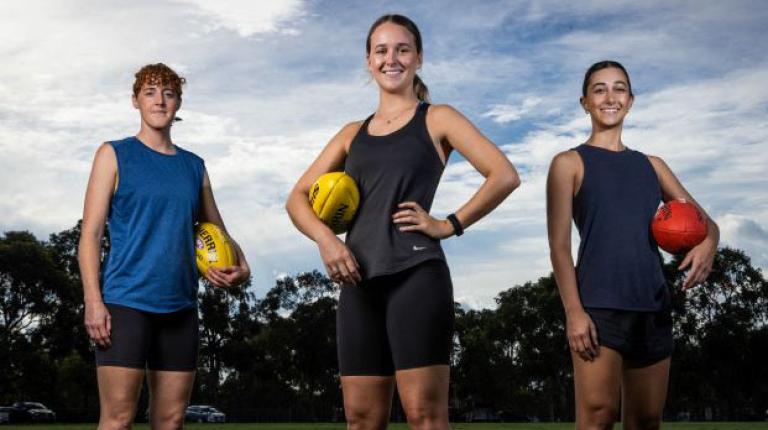 Photo courtesy Jake Nowakowski - Herald Sun Three women stand posed on a football field, each holding a football.