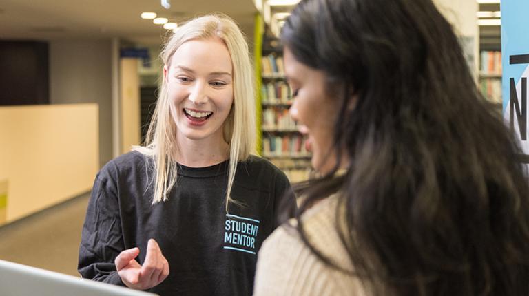 Young female university mentor, wearing a mentor shirt, smilingly offers advice to a student