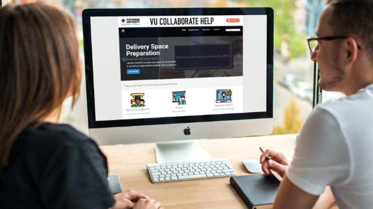 Two people sit in front of a mac desktop computer which has the VU Collaborate landing page on its screen.