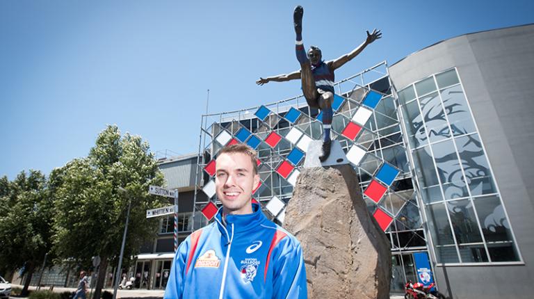 Student in Bulldogs jersey (blue) standing outside Whitten Oval courts and massage rooms.